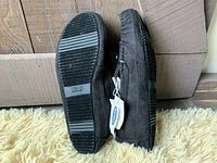 Side view of slippers showing black rubber sole with size 11-12M sticker and pair standing upright showing tags.