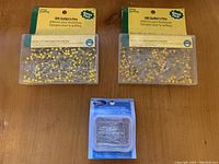 Two packs of 500 quilter's pins each with yellow pin heads and one pack of 450 long satin pins with silver finish, all new.