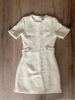 Front view of white tweed dress showing short sleeves, round neckline, fitted shape, pearl button belt detail and textured fabric.