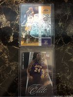 Two basketball cards featuring Kobe Bryant visible in protective sleeves, front side, placed on a dark marble surface.