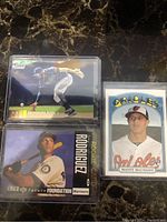 Front view of three baseball cards: Fernando Tatis Jr. chrome refractor in top-loader, Alex Rodriguez Mariners rookie card, Manny Machado Orioles vintage style card.