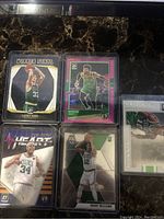 Photo of six basketball trading cards featuring Boston Celtics players including Larry Bird, Marcus Smart, Paul Pierce, and Grant Williams. Cards are in protective sleeves and arranged on dark marble surface.