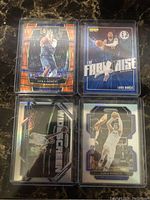 Four Luka Doncic basketball cards shown in protective holders with different designs and finishes including orange shimmer and silver variants.