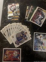 A photo showing various NHL hockey cards spread out on a surface. Recognizable players include Roy, Messier, Sakic, and Hull. Cards show players in game poses and portraits with team colors.