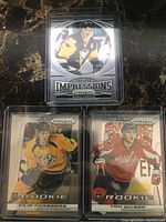 Front side of three hockey cards showing players Mario Lemieux, Filip Forsberg and Tom Wilson with Prizm branding and protective sleeves.