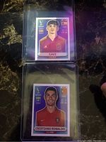 Front view of two soccer sticker cards, one of Gavi and one of Cristiano Ronaldo in protective sleeves.