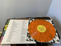 Photo of orange vinyl record with yellow center label showing the album Some Girls by The Rolling Stones and accompanying lyric insert sheet
