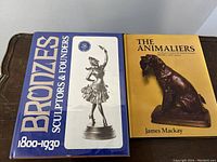 Two hardcover art books displayed side by side showing front covers, one with title 'Bronzes Sculpters & Founders 1800-1930' featuring a bronze sculpture of a ballerina, the other 'The Animaliers' by James Mackay showing a bronze dog sculpture.