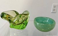 Photo showing two different Murano glass bowls: one abstract green bowl with flowing folds, one smaller round green speckled bowl