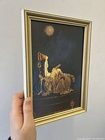 Photo of the framed artwork held upright showing the front view with the figure in a seated position and background details visible.