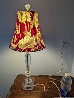 Full view of the lamp lit on a wooden surface showing its cut crystal base and floral fabric shade.