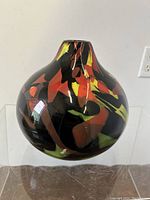 Front view of round Murano glass vase showing vibrant red, yellow, and orange patterns on black glass.
