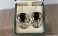 Pair of silver earrings with black onyx stones resting in a vintage box with cushioned lining.