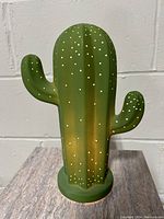 Front of green ceramic cactus lamp showing small perforations and two arms.