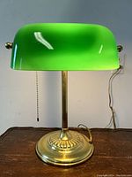 Front view of the brass base bankers lamp showing emerald green glass shade and pull chain.