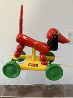 Side view of the red wooden dachshund pull-toy with green wheels and yellow base showing the BRIO Made in Sweden label.