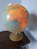 Front view of the illuminated globe showing the continents and the gold-tone base.