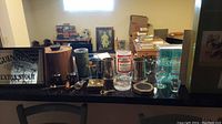 View of assorted barware items including Guinness ice bucket, various glassware including steins and stemware, coasters, ashtrays and wine cork pullers on counter.