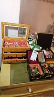Two wooden jewelry boxes on a dresser surface with various costume jewelry inside and around, photo showing overall lot contents.