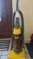 Full upright view of Eureka vacuum cleaner showing yellow and gray colors and attached hose.
