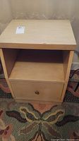 Front view of vintage light wood nightstand showing top surface, open middle shelf, and bottom drawer with metal knob.
