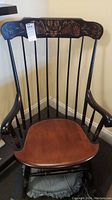 Full view of wooden rocking chair with varnished wood seat and black spindles, showing overall condition and design.