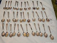 Top view of full 34-piece Wm. Rogers Co. silverplate presidential spoon set laid out on a cloth, spoon handles showing presidential motifs.