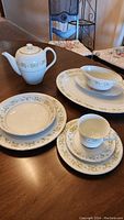 Dinnerware set including teapot, layered plates, cup and saucer on wooden table, showing Royal Hostess Bridgit pattern of green floral design with gold trim