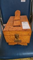 Closed wooden shoe shine box with handle on top placed on a chair.