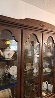 Cabinet with multiple items including stemware, Wedgwood items, vases, teapots, and decorative bowls visible inside the glass doors.