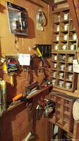 Wooden wall with mounted tools including hammers, drill, clamps, multiple small tins containing hardware items organized in wooden shelving.