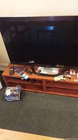 Front view of LG 47in TV on wooden stand with remotes and DVDs on floor in front