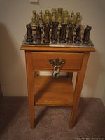 Chess set arranged on wooden side table with drawer, lock securing drawer, showing full view of table and chess pieces standing on the board.