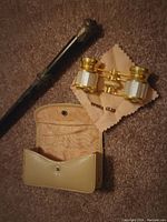 Photo showing the ebony conductor's wand and brass opera glasses with mother of pearl accents, along with the beige case.