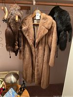 All three items hanging on rod: pastel mink coat center, brown fox wrap left, black mink wrap right