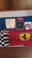 Overview of all items laid out on blue surface: Ferrari flag, signed plate, team towel and puck, pencil sketches