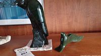 Wide shot of both jade carvings: tall perched bird sculpture and smaller stylized bird carving on wooden shelf