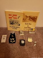 Overview photo displaying two books, multiple raw silver-colored mining samples on a black velvet PEZ pouch, resin-encased mining samples, and small labels on a carpeted surface.