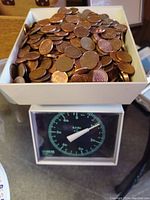 Circulated pennies in white tray on coin counting scale showing weight.