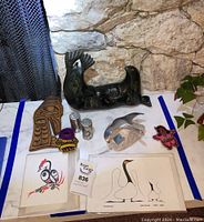 Overview of entire lot on marble surface, including repaired stone sea lion sculpture, pewter bird on rock, Native wood carving, salt and pepper shakers, two bird prints, and colorful patches or pins.