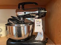 Vintage Sunbeam Mixmaster chrome stand mixer with one stainless steel bowl placed on base, side view with item tag attached.