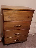 Front view of tall boy dresser showing four drawers with metallic handles and wooden finish.