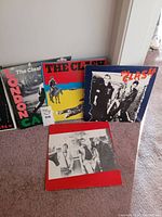Four vinyl record albums arranged on carpet including three by The Clash and one D.O.A. album in front.