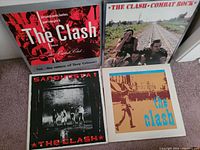Four vinyl album covers from The Clash on carpet, showing different album art for each including red and black illustrated cover, railway photo, black and white photo with red text, and beige cover with blue text.