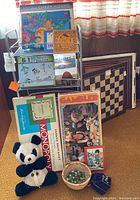 Overview of lot contents showing Monopoly box, framed chess board, balloon art kit, solar kit, panda plush, basket with marbles and vintage car on cart