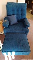 Front view of the blue upholstered chair with visible cushioned seat, backrest, armrests, and small matching pillow on the seat.