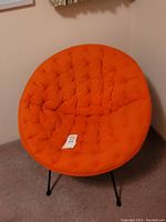 Front view of orange cushioned saucer chair showing round seat and black metal legs