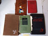 Top view showing six cookbooks of varying sizes and covers including wood-bound Chinese and red Rumford cookbooks.