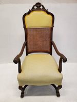 Front view of antique armchair showing yellow upholstered seat and caned back with carved wood frame
