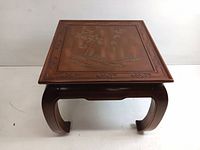 Front view of wooden square side table with carved bird and foliage engraving and bow-shaped legs.